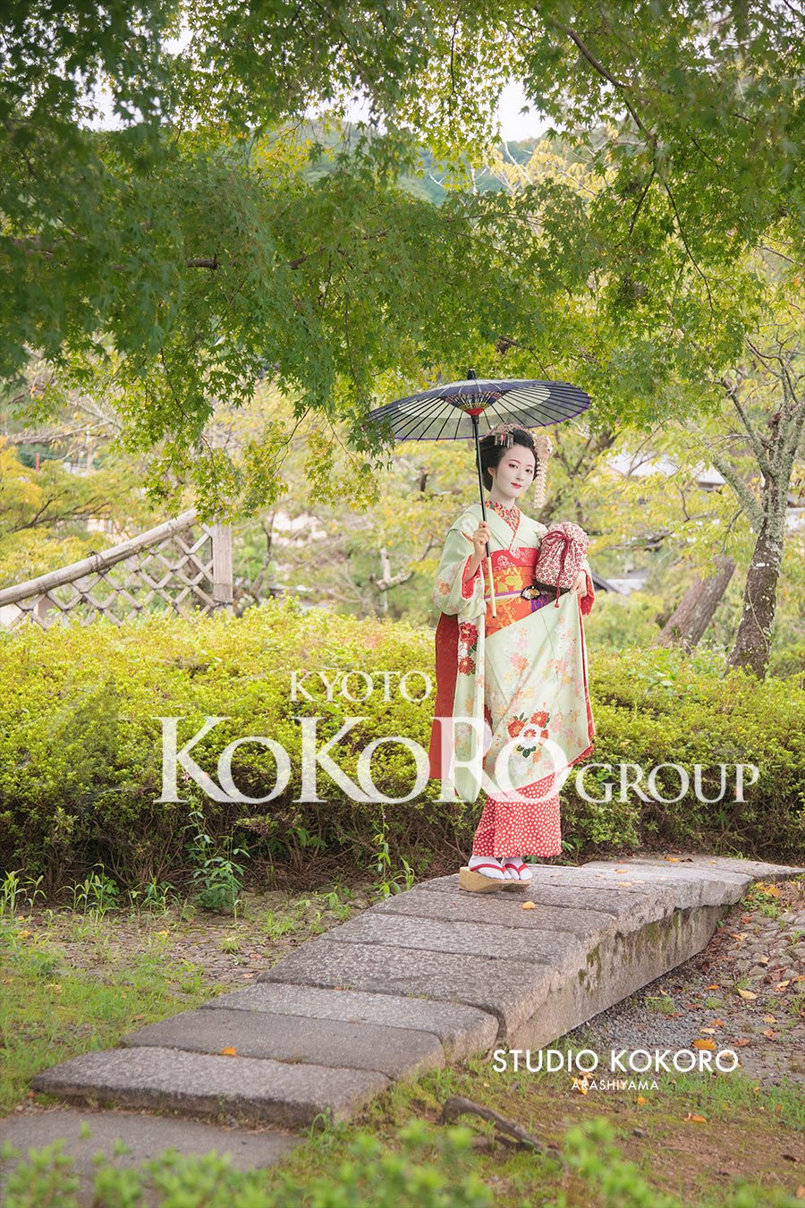 嵐山の緑豊かな公園と青紅葉を背景にした舞妓姿のお客様